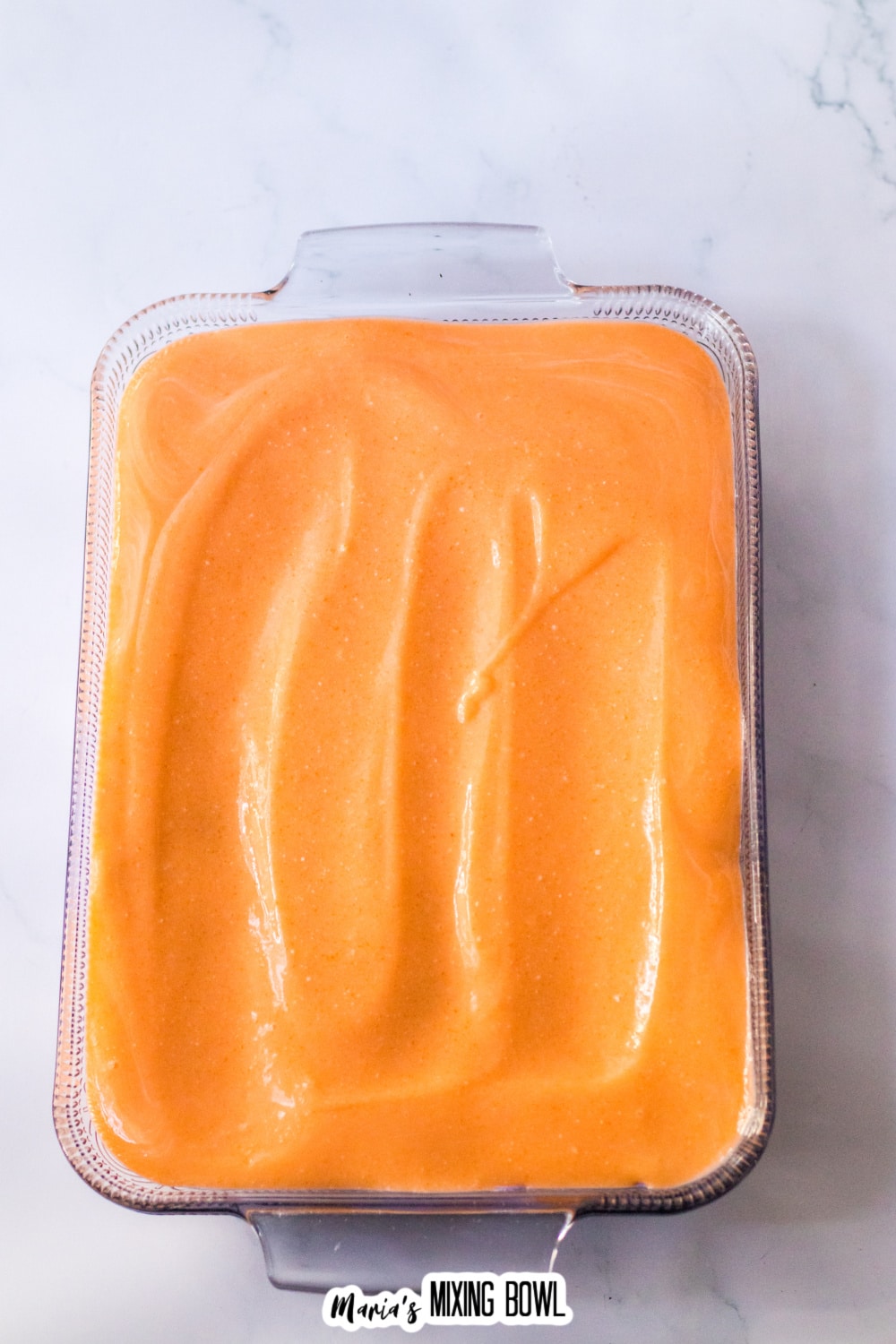 orange pudding layer being spread on top of a glass baking dish.