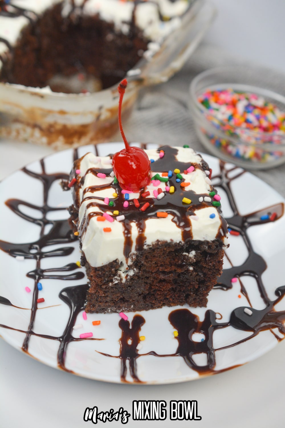 slice of hot fudge poke cake on a plate with a cherry on top.