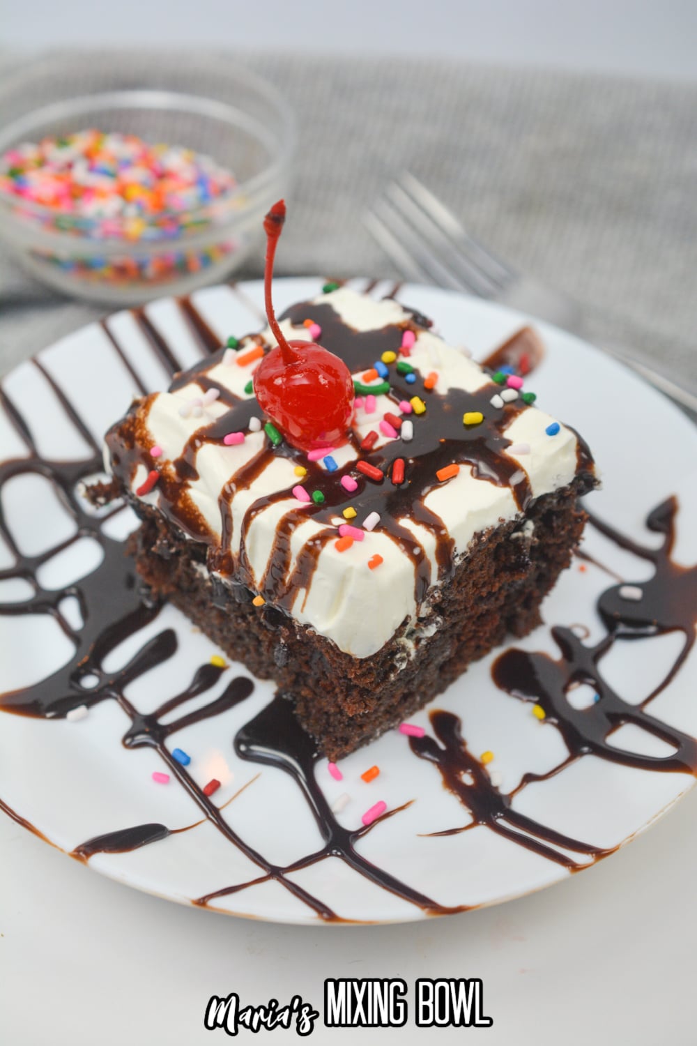 slice of hot fudge poke cake on a plate with a cherry on top.