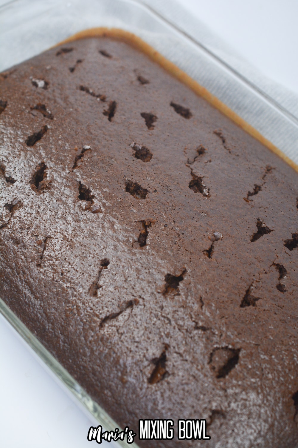 holes being poked into a baked chocolate cake in a glass baking dish.