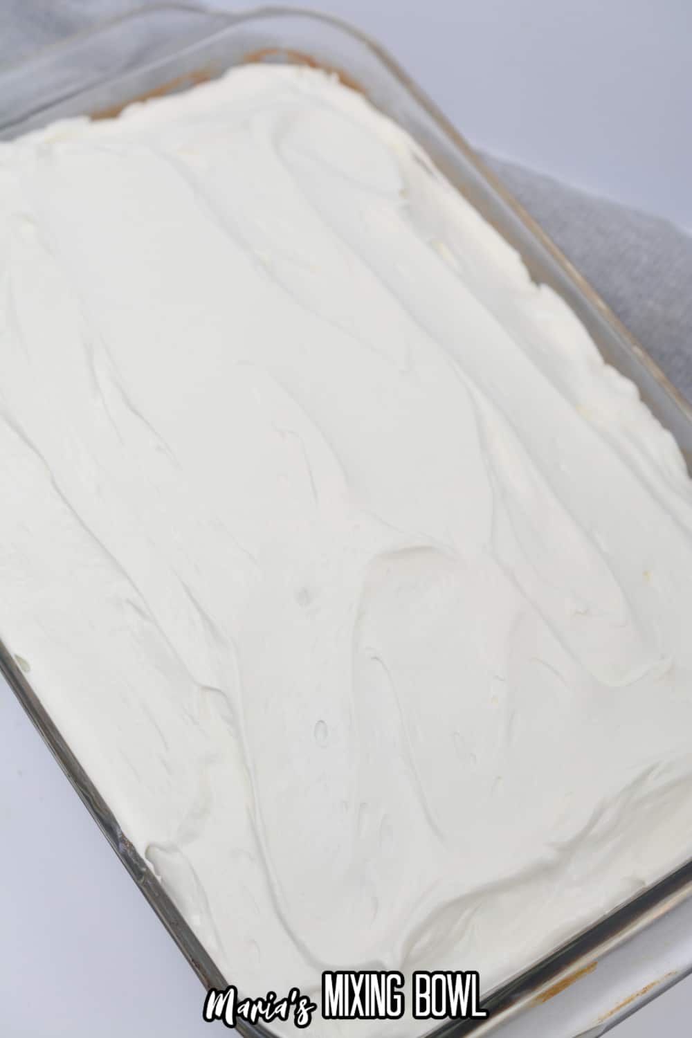 whipped topping being spread over the top of a chocolate cake in a glass baking dish.