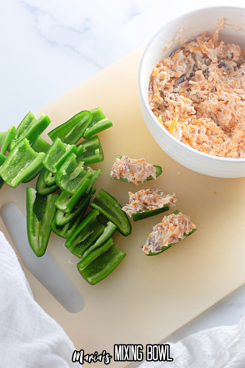 cream cheese and bacon mixture being stuffed into pieces of jalapeno peppers.