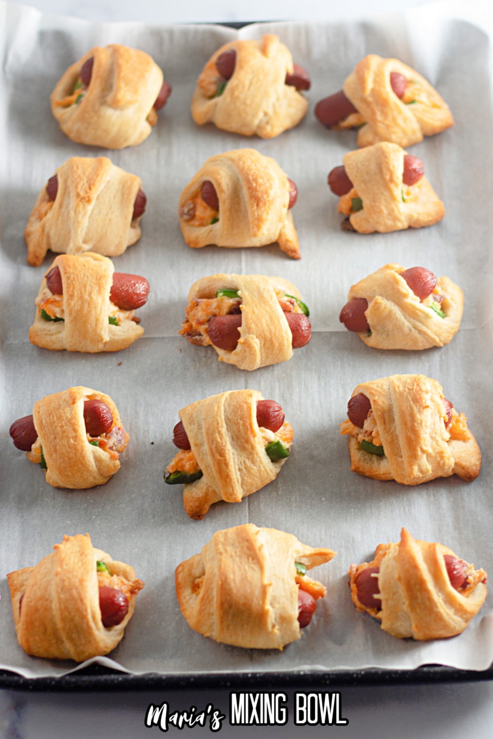 cooked jalapeno crescents pigs in a blanket on a parchment lined baking sheet.