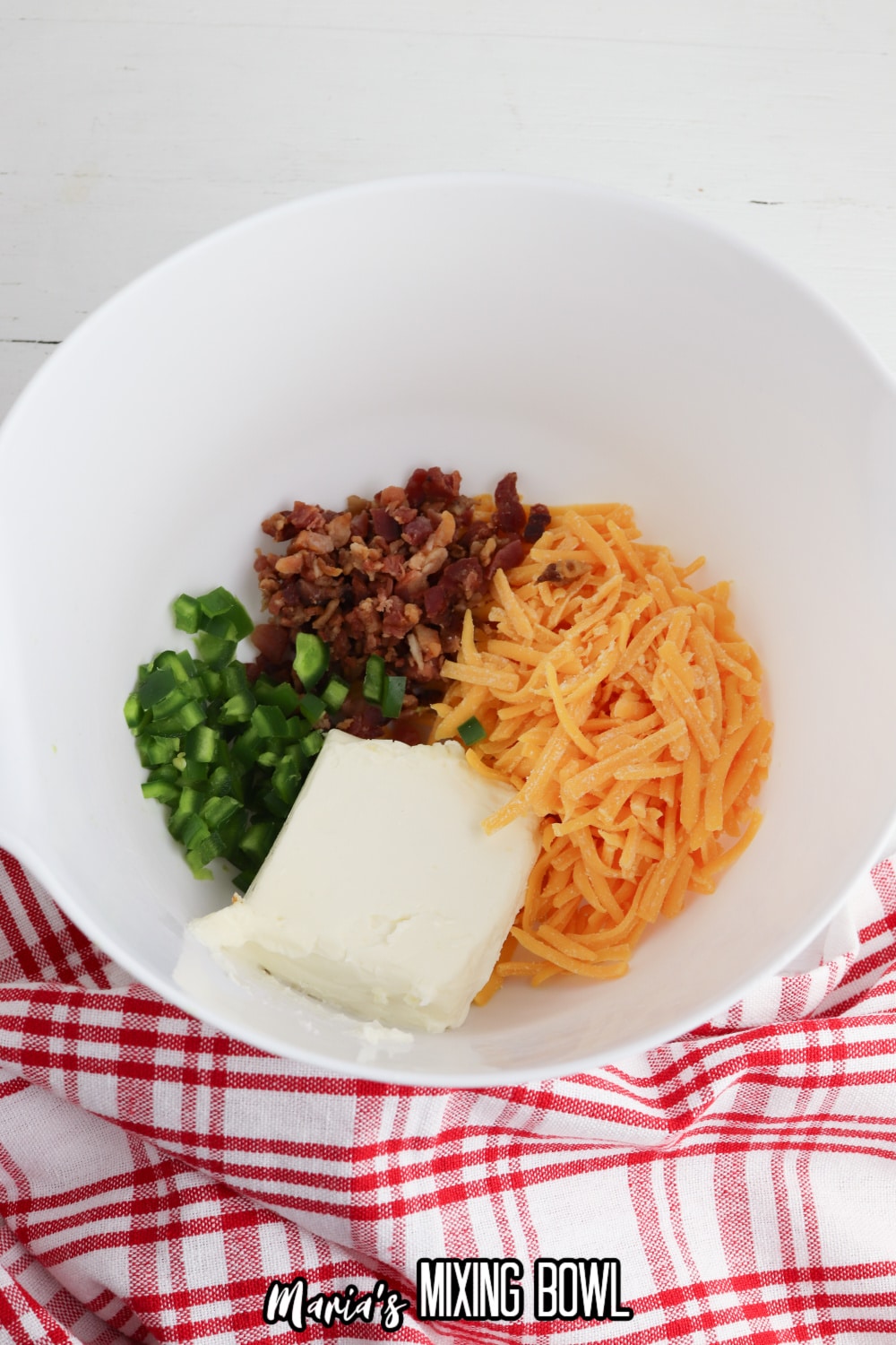 large bowl filled with diced jalapenos, cream cheese, shredded cheddar cheese, and cooked bacon.