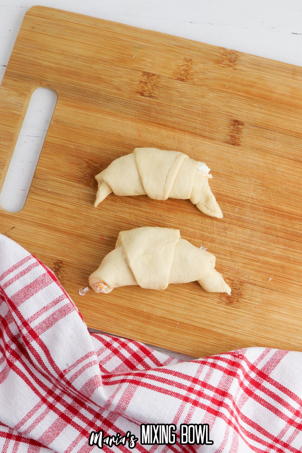two stuffed crescent rolls on a wooden cutting board.
