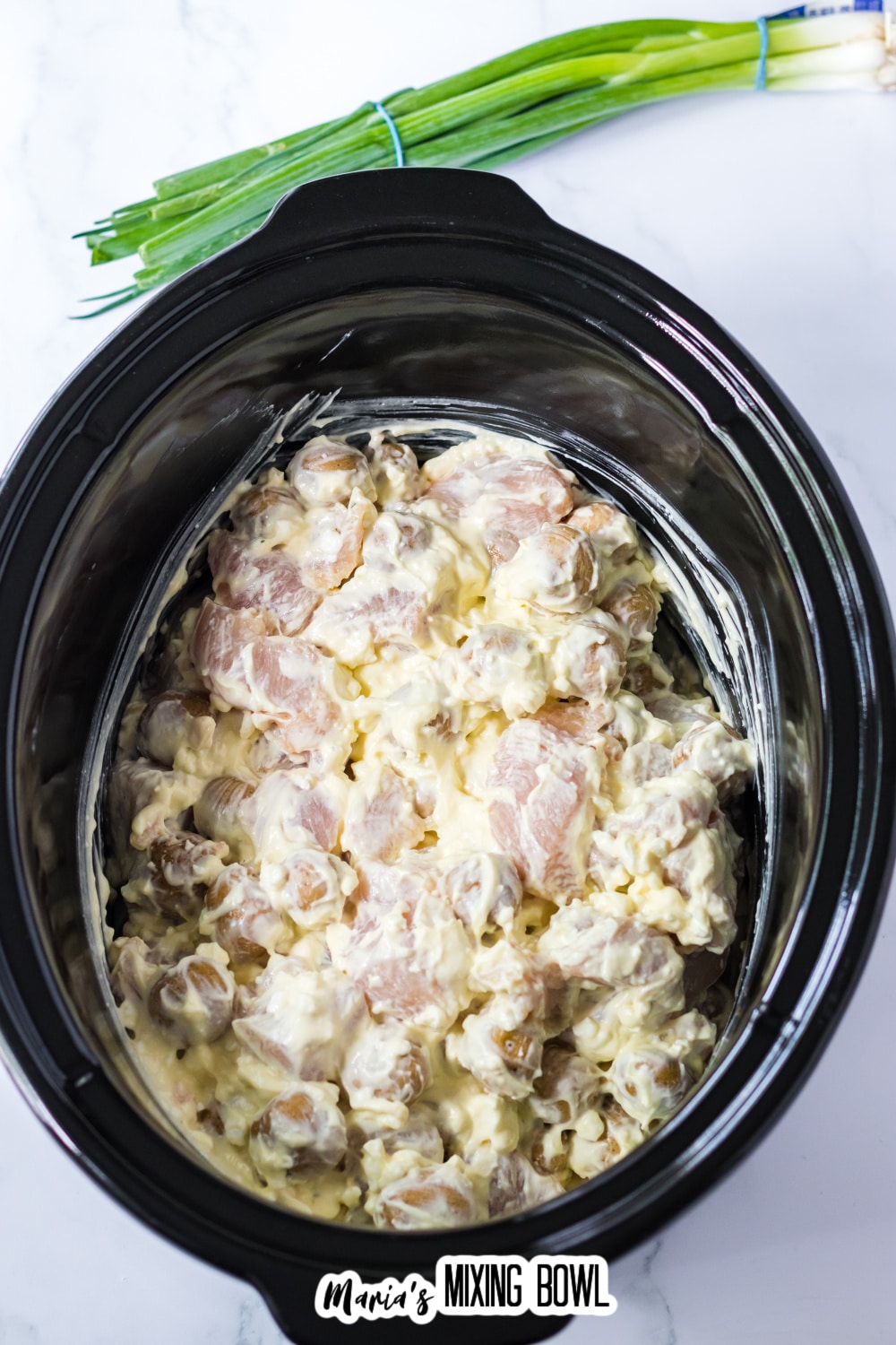 raw chicken and potatoes coated in a creamy sauce in a slow cooker.