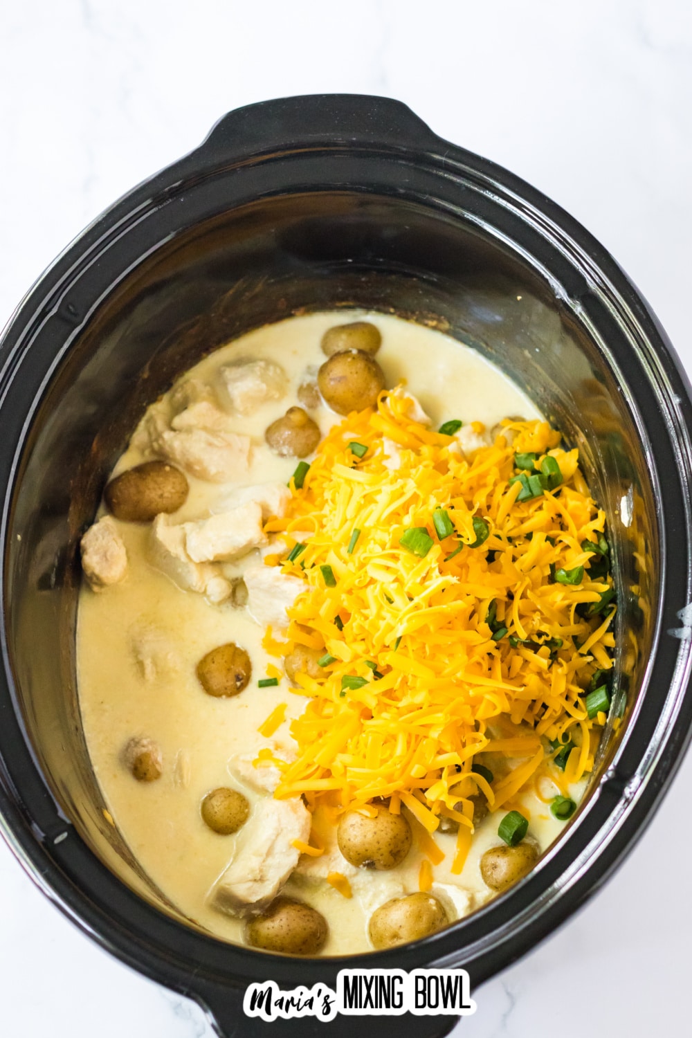shredded cheese, green onions, potatoes, and chicken in a slow cooker.