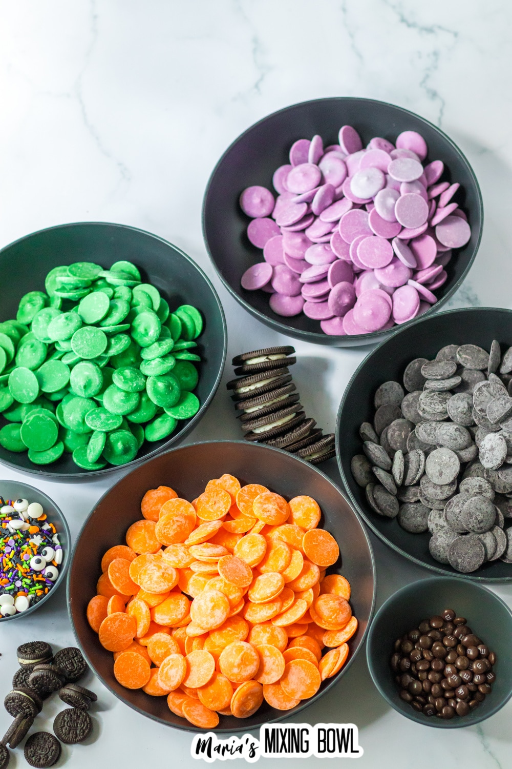 bowls of purple, green, orange and black candy melts. Plus oreo cookies, and sprinkles.