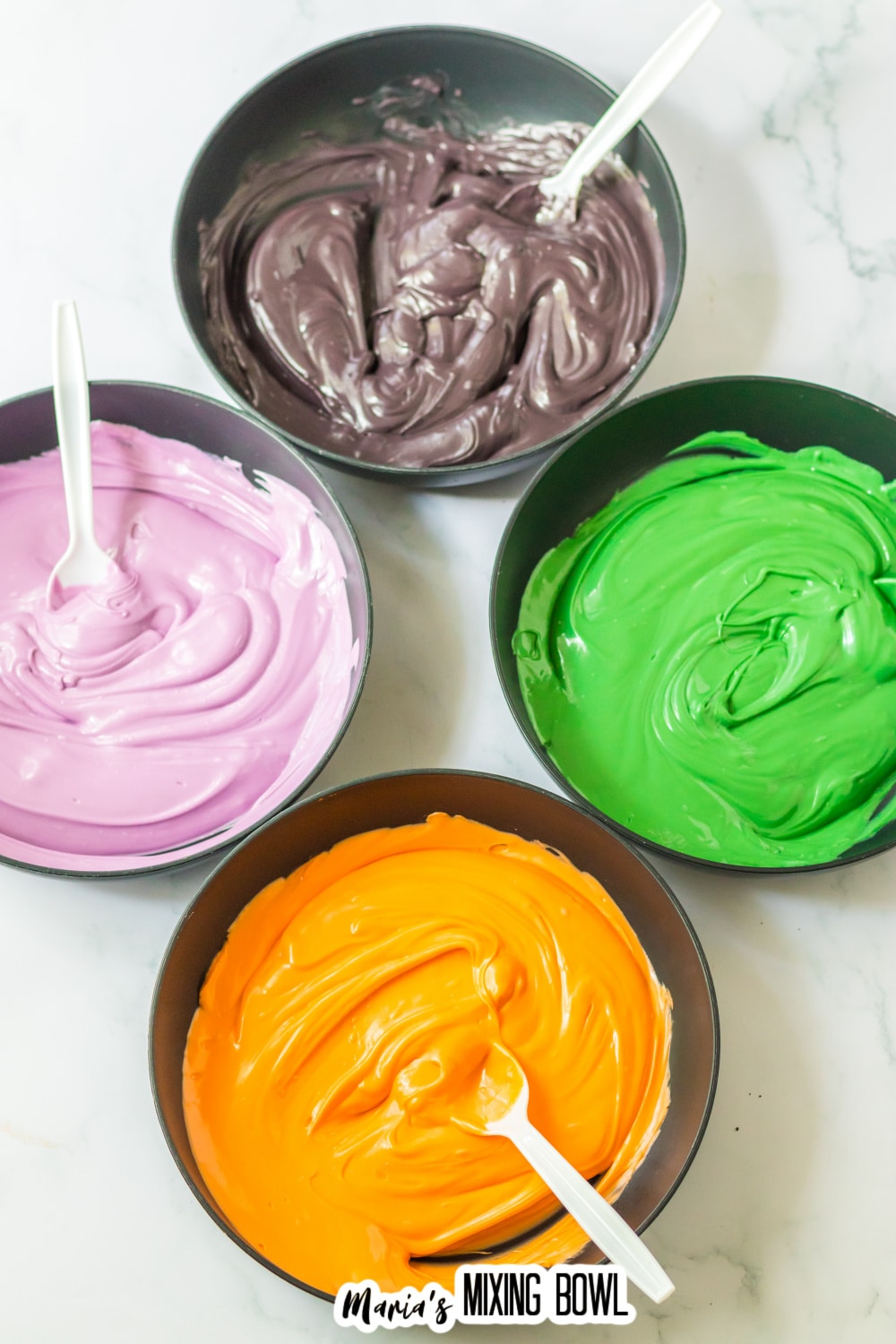 bowls of purple, green, orange, and black melted candy melts.