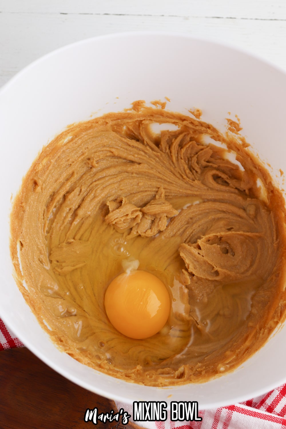 mixture of peanut butter and sugar in a mixing bowl with a raw egg being added to it.