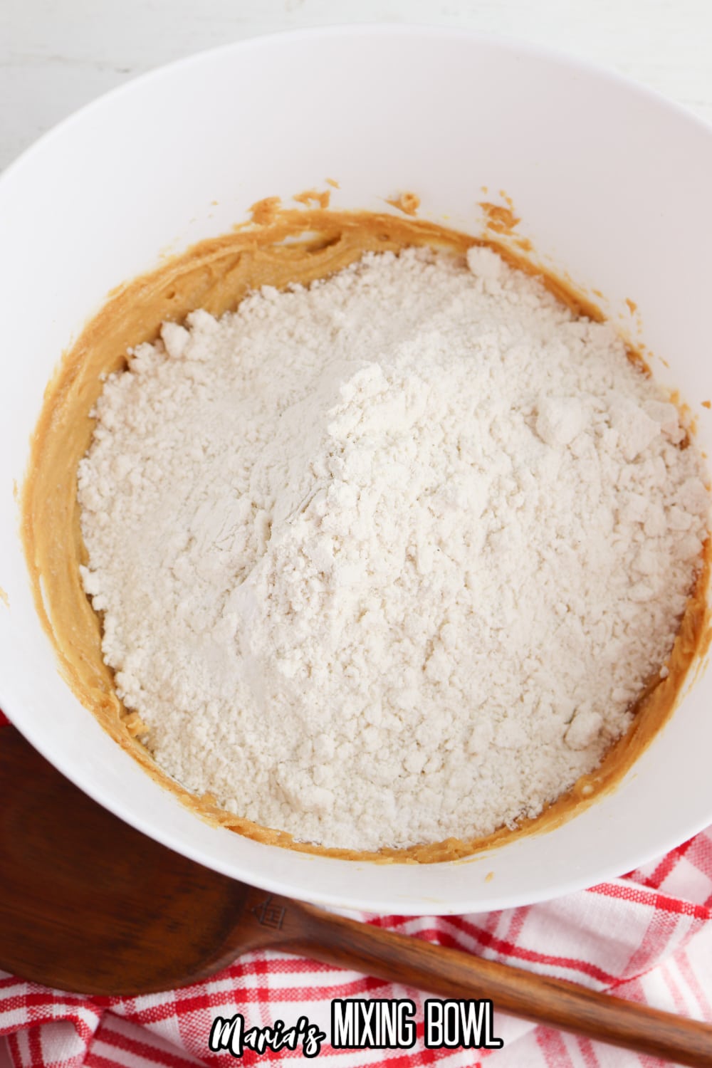 flour being added to a peanut butter, eggs, and sugar in a large bowl.