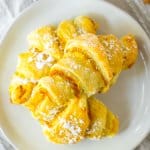 three pumpkin pie crescent rolls stacked on a white plate.