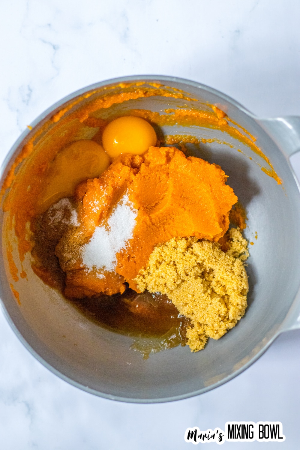 stainless steel mixing bowl filled with pumpkin, eggs, and sugar.