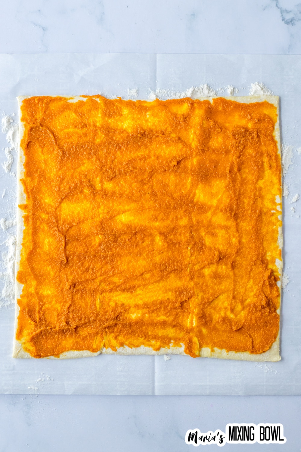 pumpkin pie mixture being spread in a thin layer on top of a sheet of puff pastry.