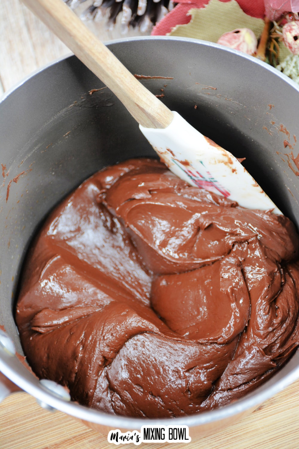 chocolate fudge being stirred with a rubber spatula in a stainless steel mixing bowl.