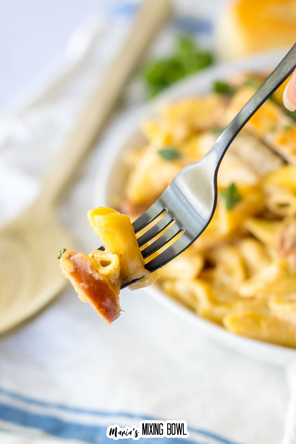 bite of pasta and smoked sausage held on a fork in the air.
