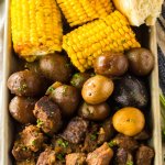 metal tray filled with beef tips, cooked potatoes, and corn on the cob.