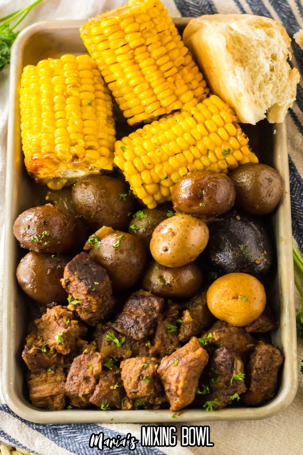 metal tray filled with beef tips, cooked potatoes, and corn on the cob.