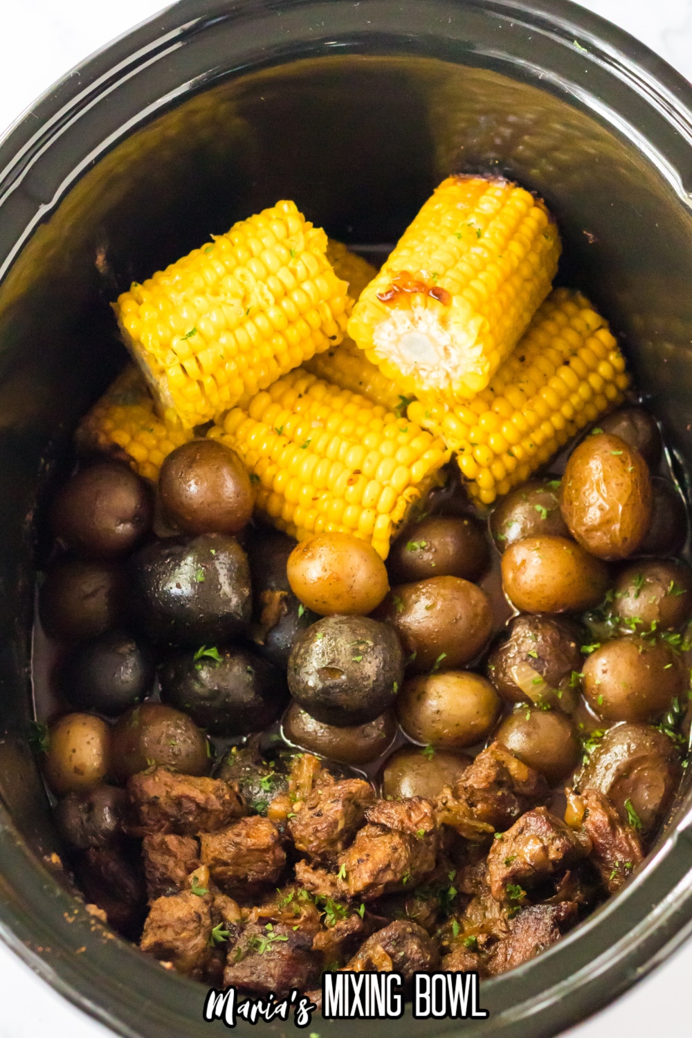 cooked steak, potatoes, and corn on the cob in a slow cooker.