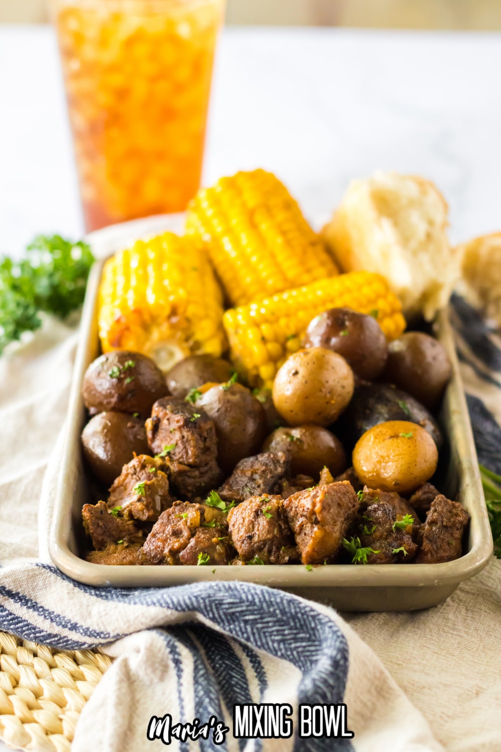metal tray filled with beef tips, cooked potatoes, and corn on the cob.