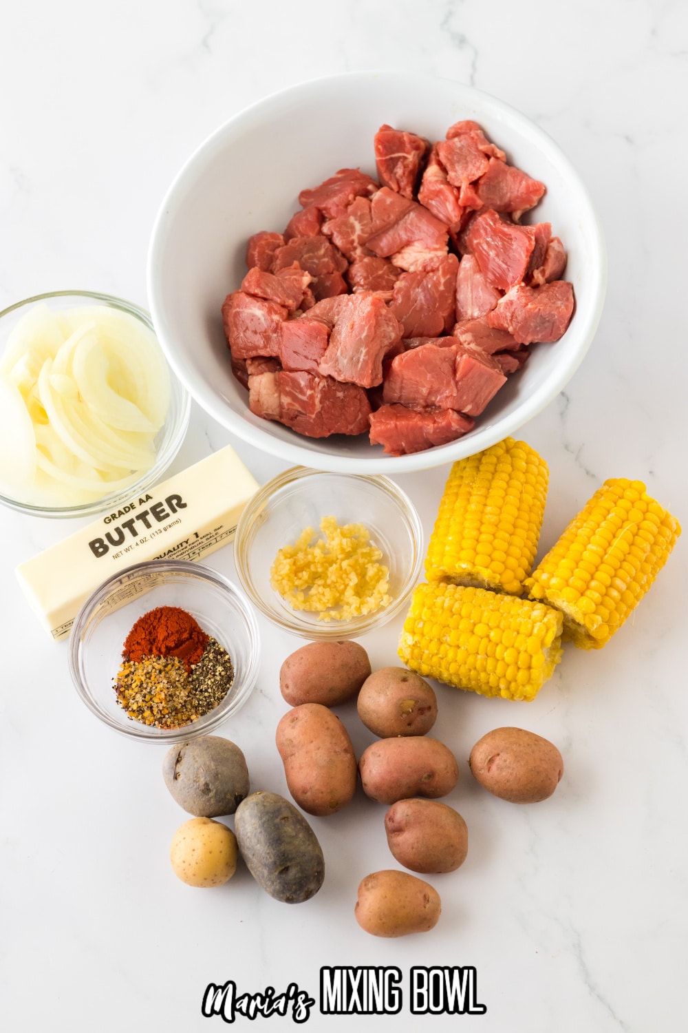 bowls of steak bites, onions, butter, corn on the cob, potatoes, garlic, and seasonings.