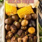 metal tray filled with beef tips, cooked potatoes, and corn on the cob.