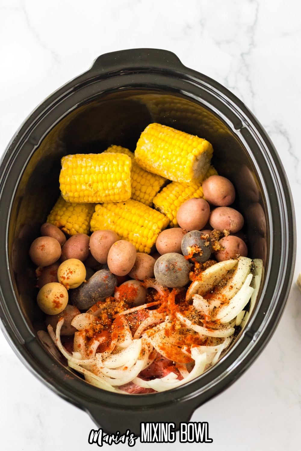 mini corn on the cob, whole baby potatoes, stew meat, onions, and seasonings in a slow cooker.