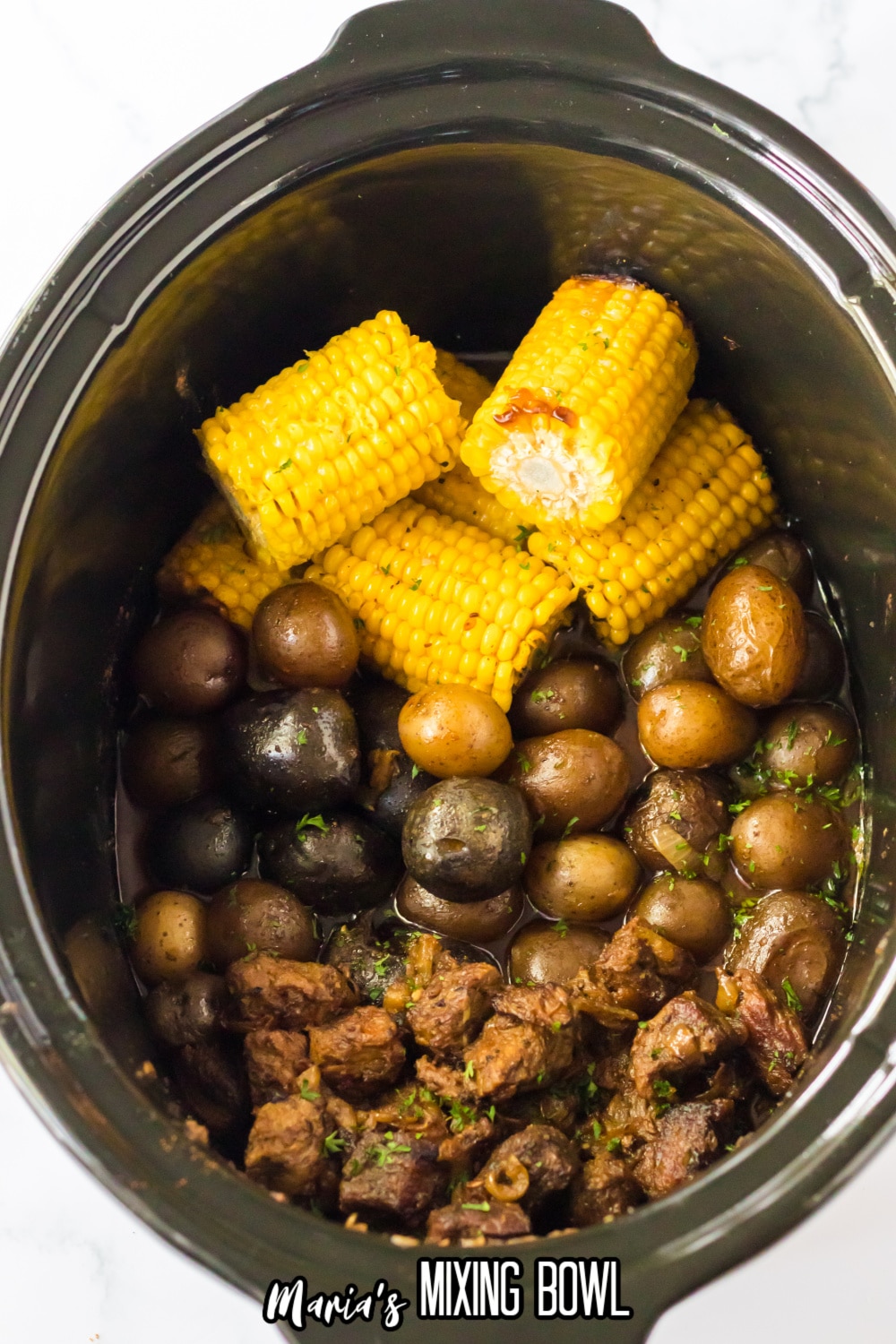 cooked steak, potatoes, and corn on the cob in a slow cooker.