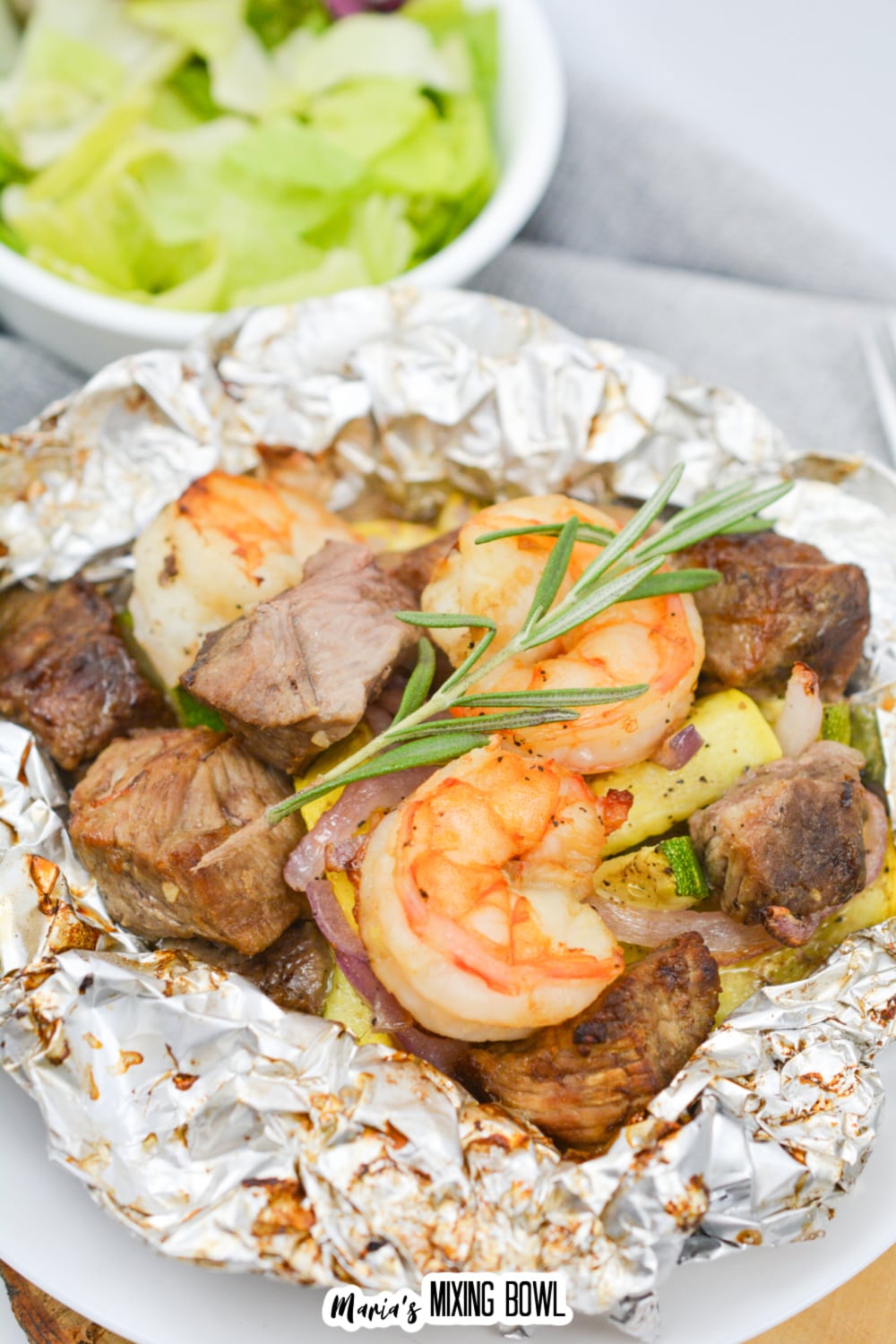 opened foil packet filled with steak, shrimp, and cooked vegetables.