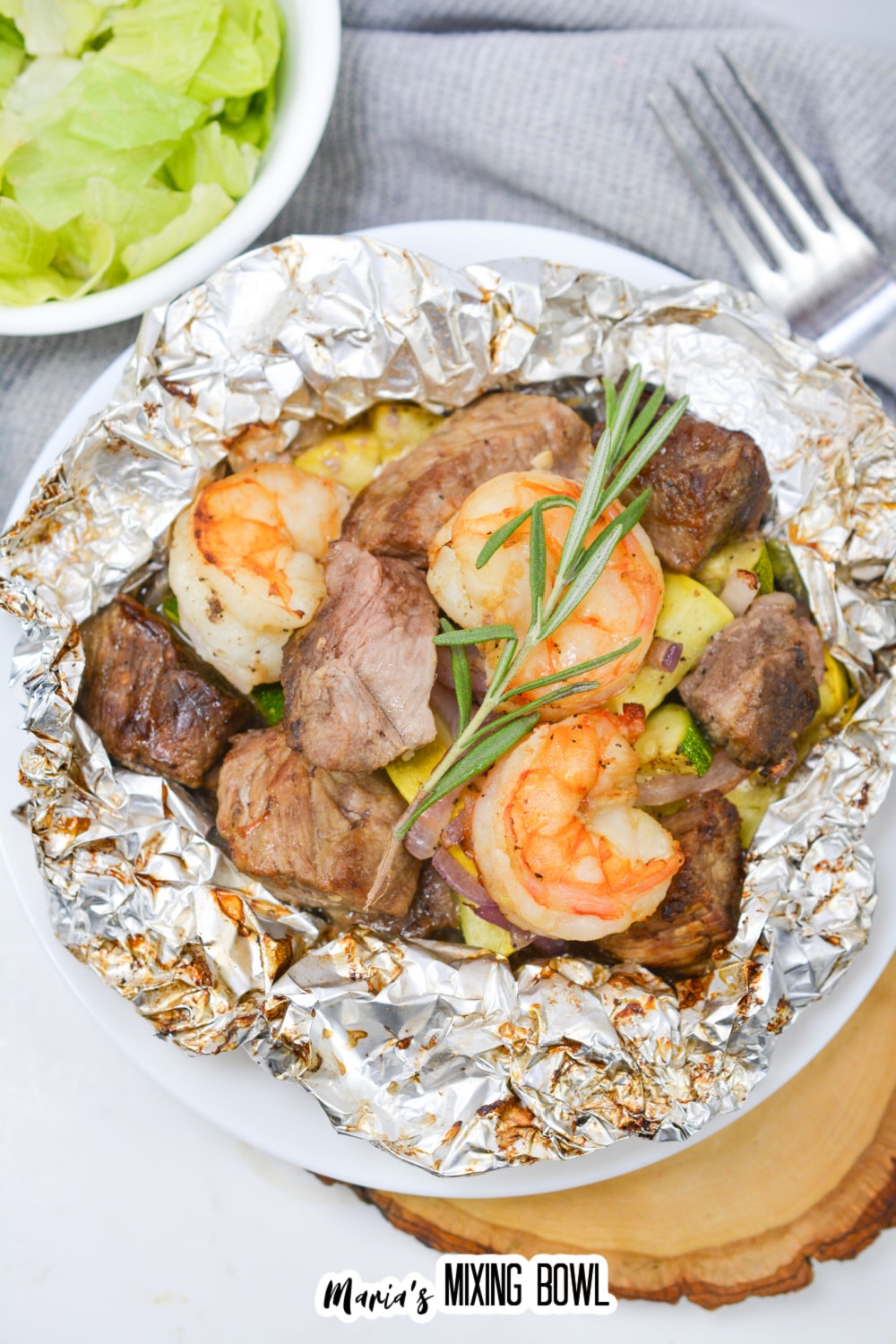 opened foil packet filled with steak, shrimp, and cooked vegetables.