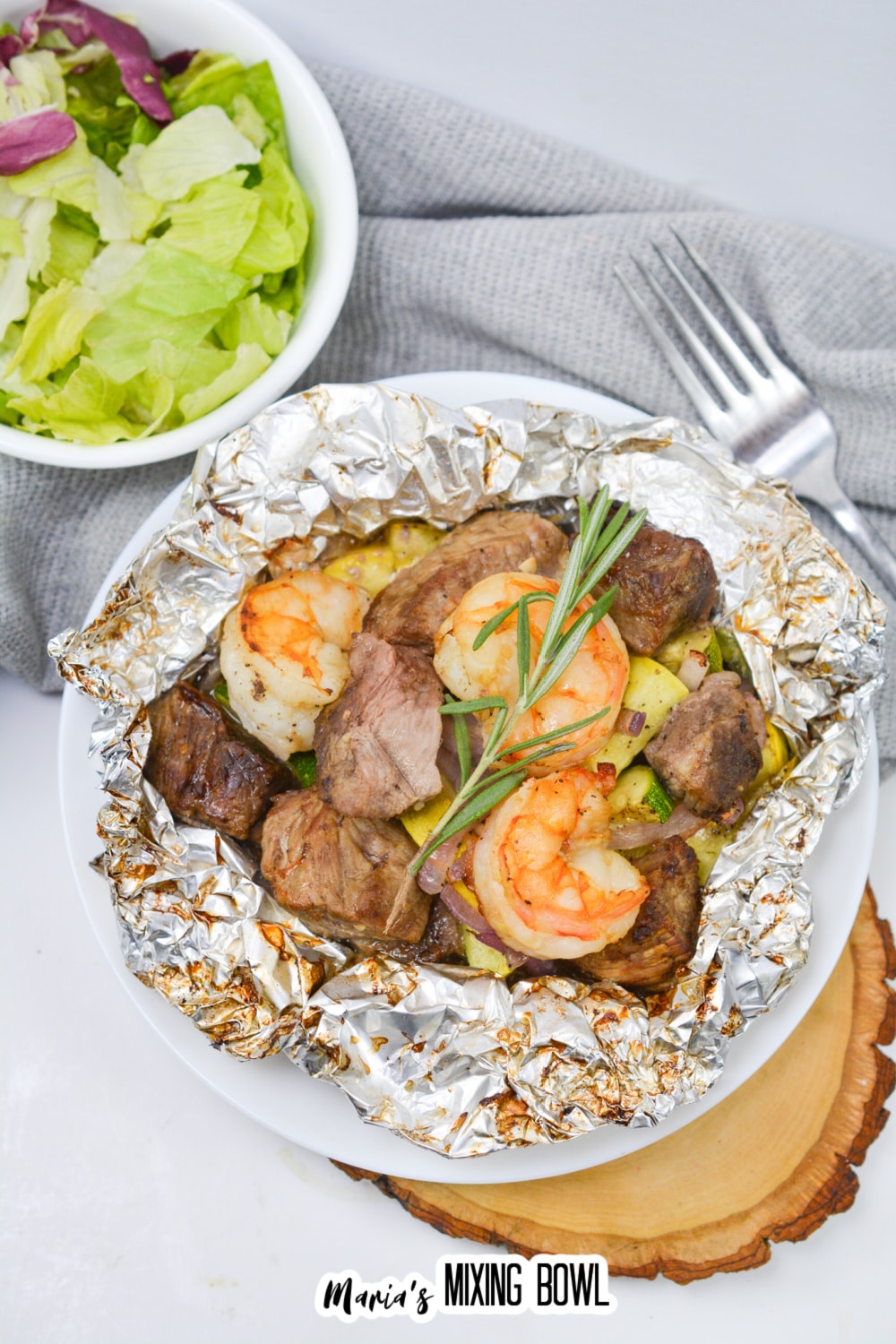 opened foil packet filled with steak, shrimp, and cooked vegetables.