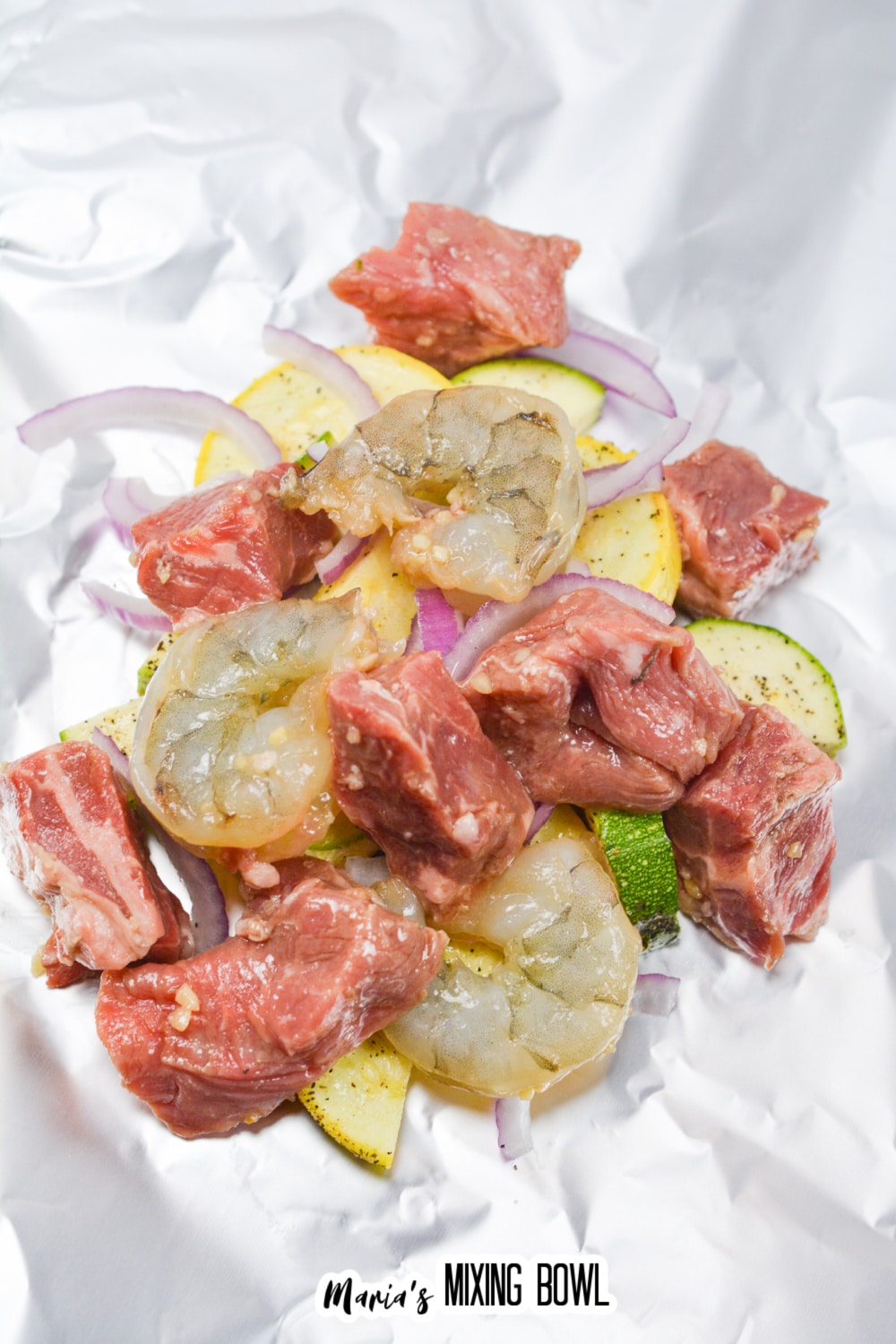 raw vegetables, raw steak, and raw shrimp being added to a foil packet.