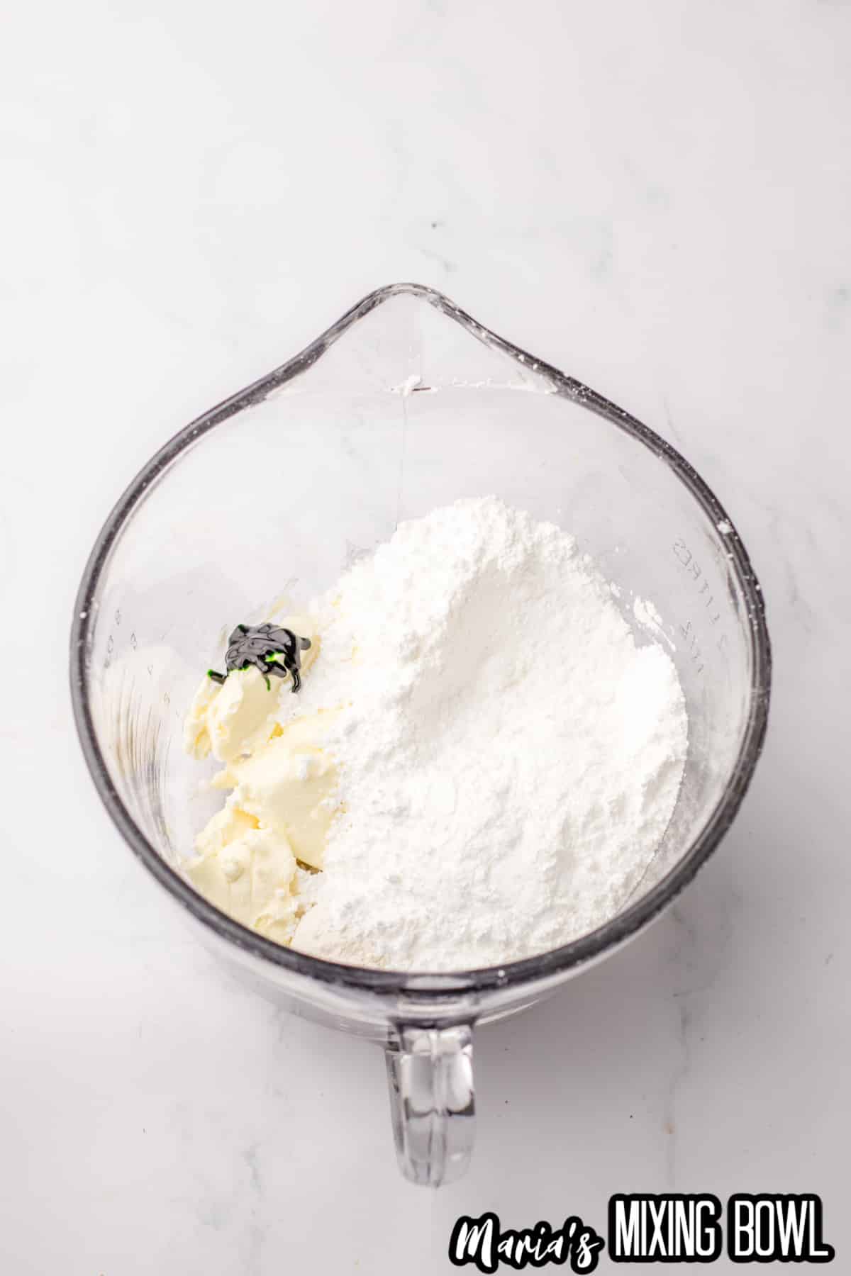 butter, sugar, and black food dye being creamed together in a glass mixing bowl.