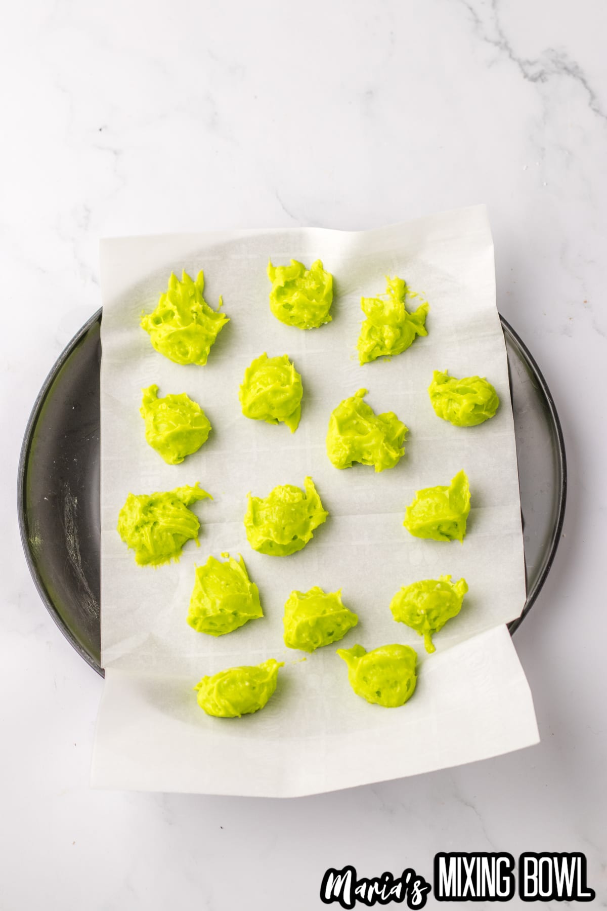dollops of green colored cheesecake mixture balls on a parchment lined plate.
