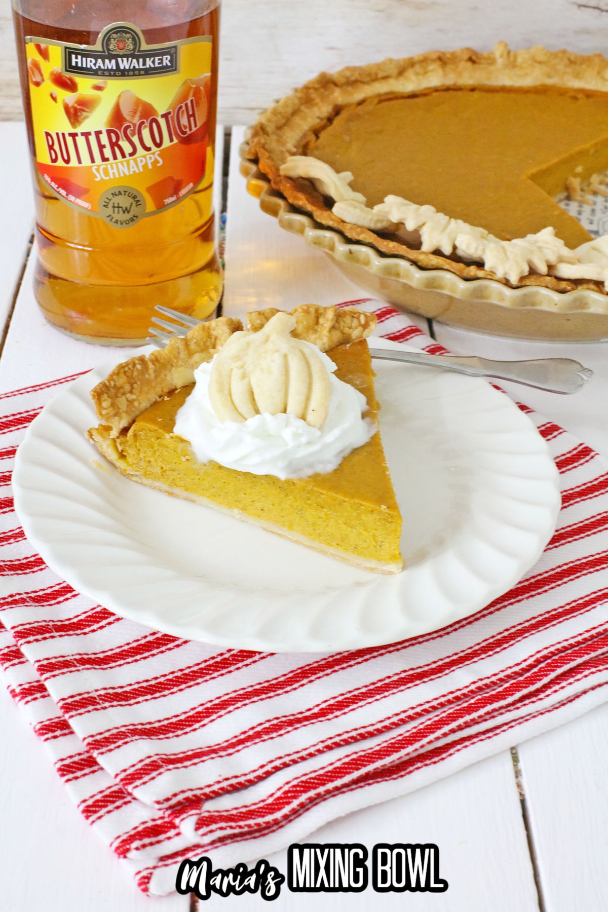 slice of boozy pumpkin pie topped with whipped cream on a plate.