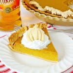 slice of boozy pumpkin pie topped with whipped cream on a plate.