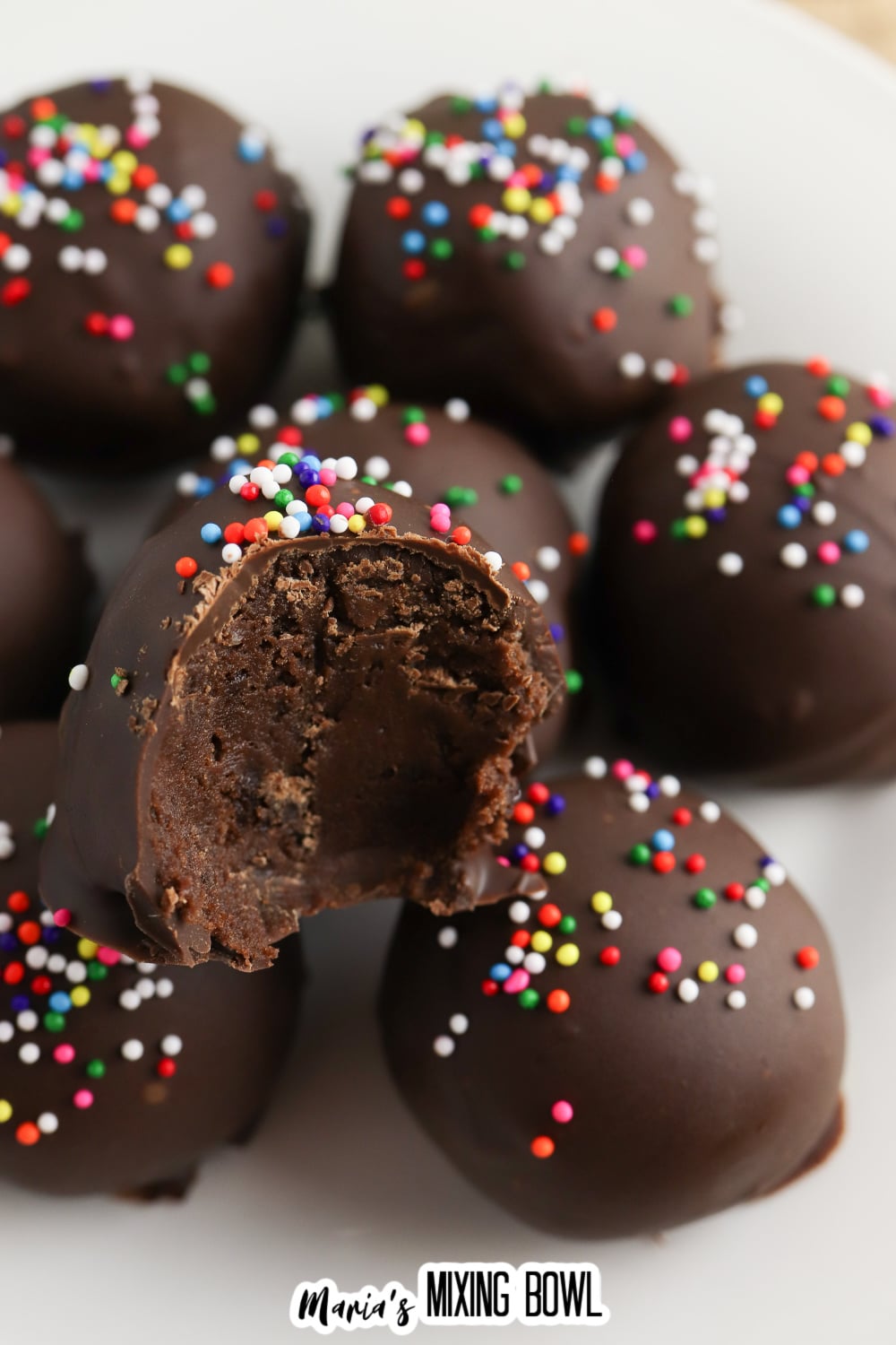 stack of brownie truffles on a white plate, the top one has a bite missing.