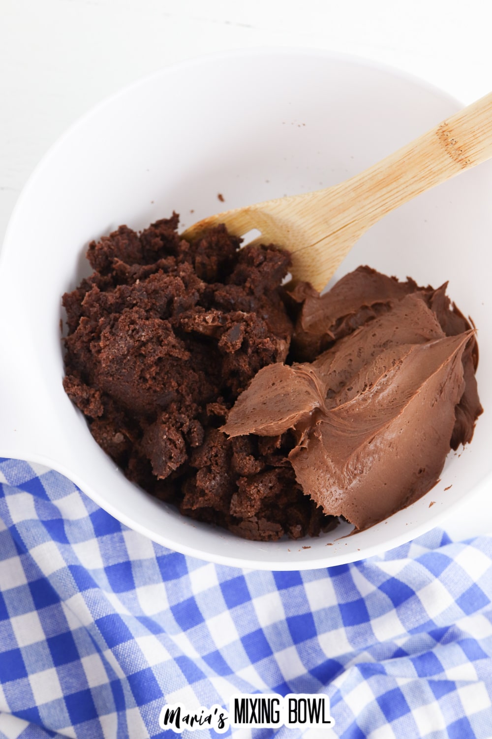 crumbled brownie and chocolate frosting being mixed together in a bowl with a wooden spoon.