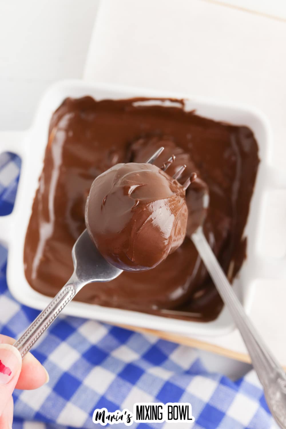 brownie truffle being dipped in melted chocolate with a fork.