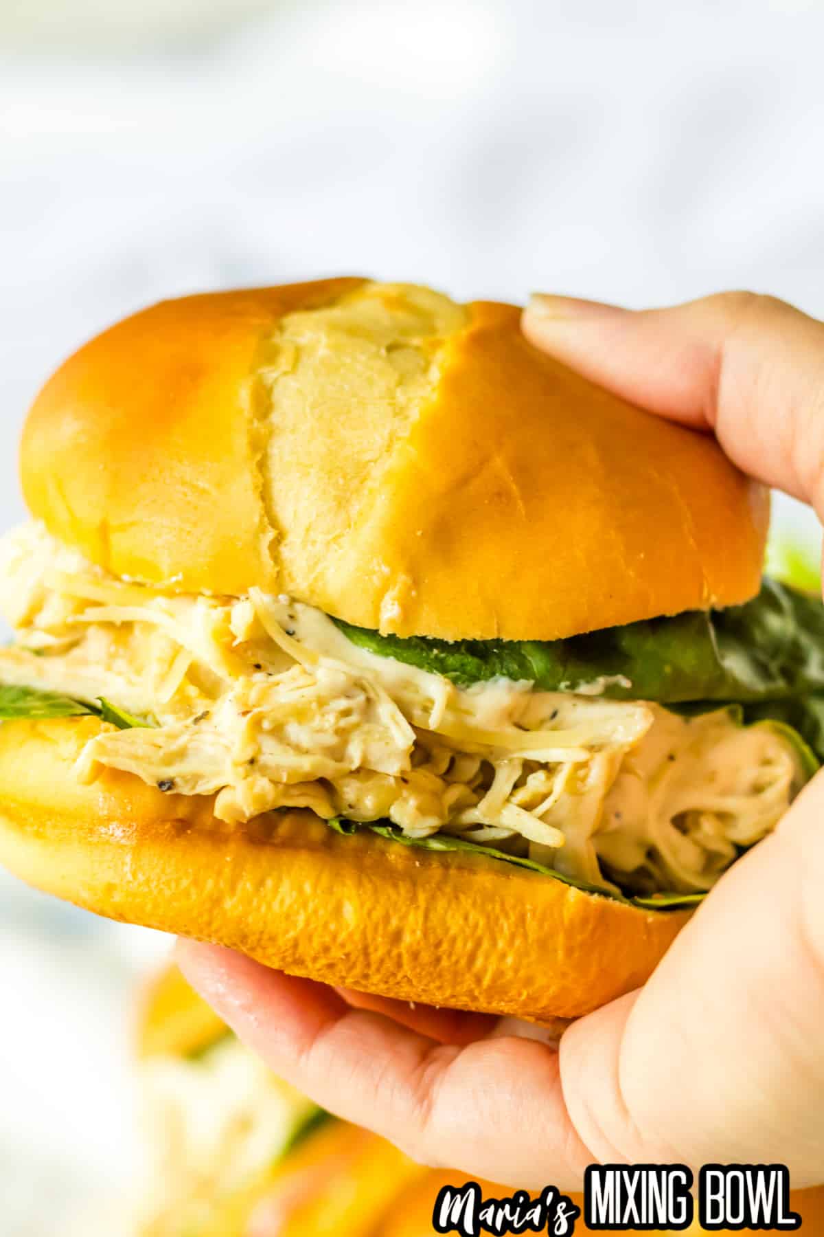 chicken ceasar sandwich held in the air in a woman's hand.