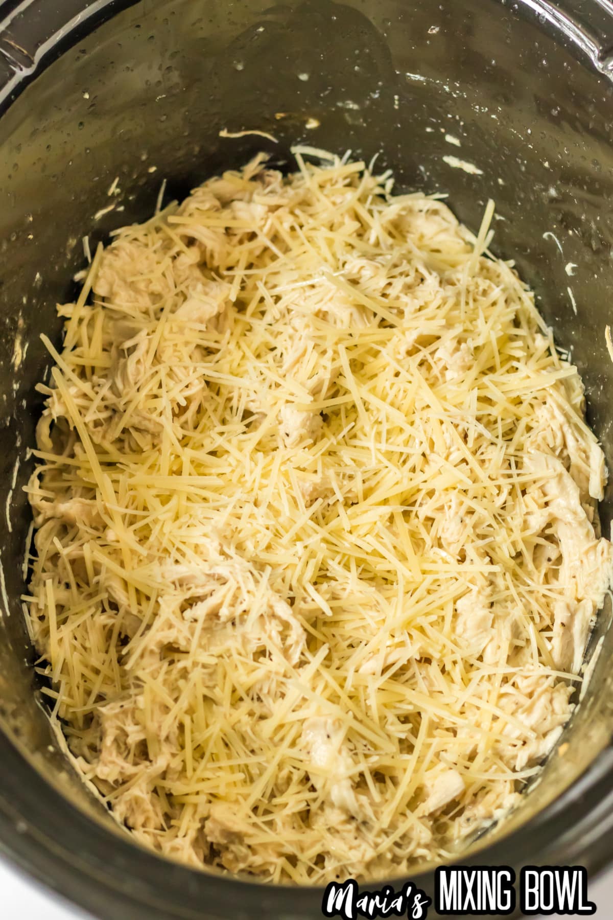 shredded parmesan cheese being added to shredded chicken in a slow cooker.