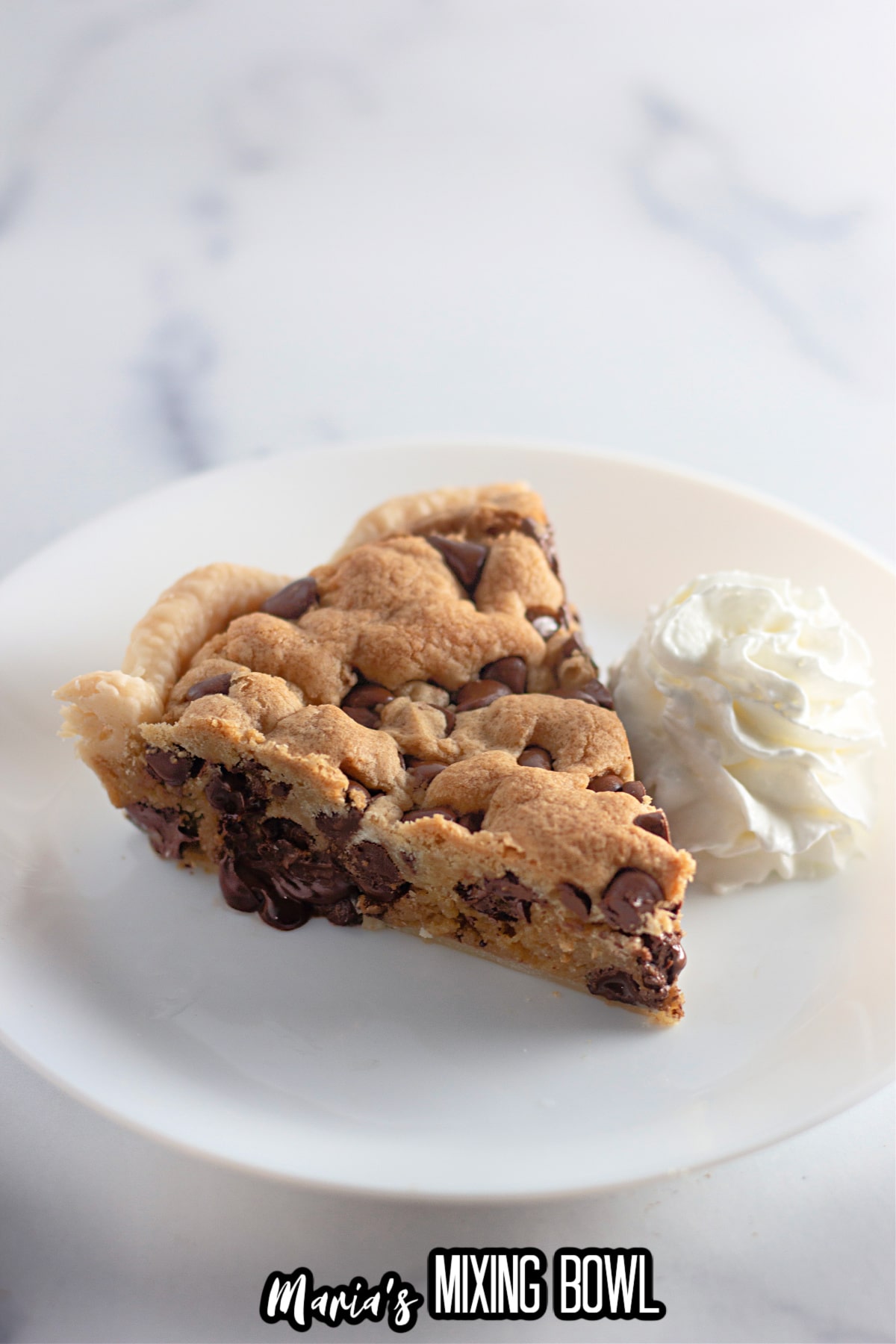 slice of chocolate chip cookie pie on a plate with a dollop of whipped cream next to it.