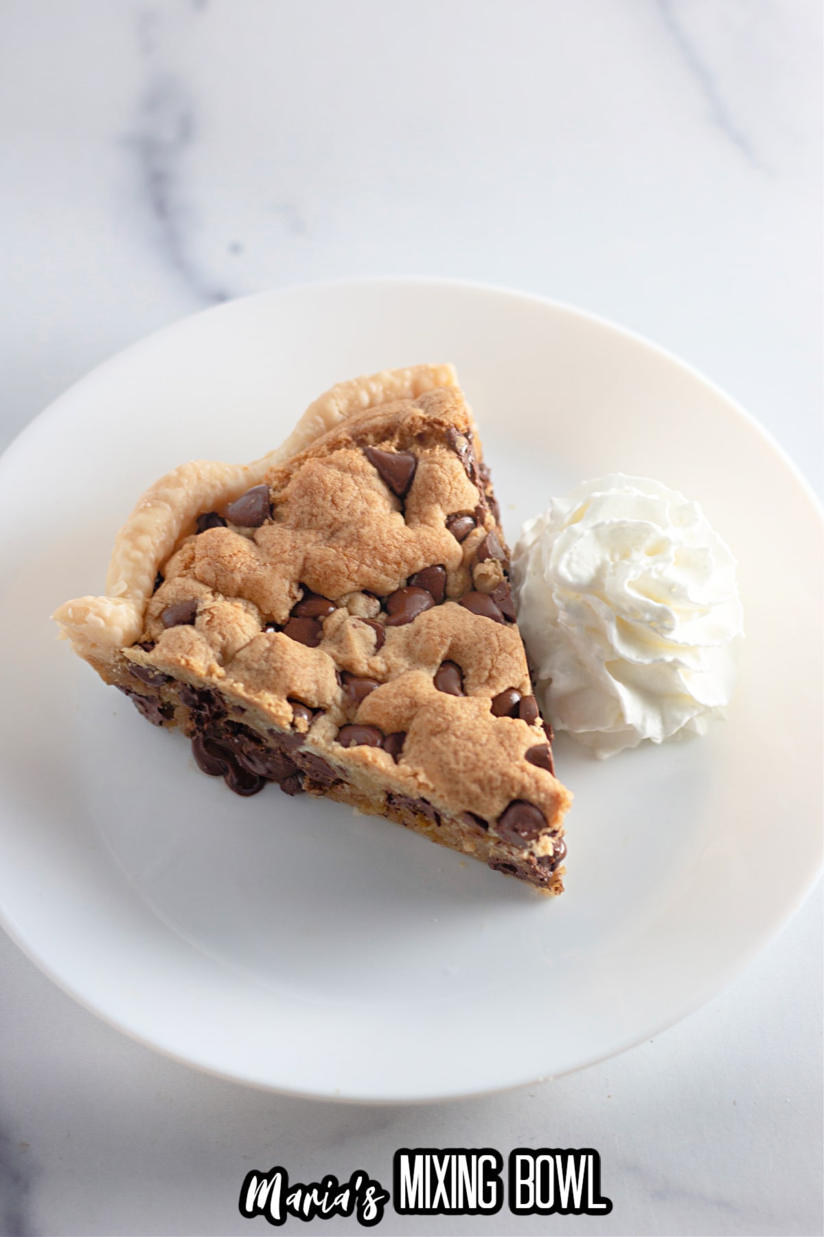 slice of chocolate chip cookie pie on a plate with a dollop of whipped cream next to it.