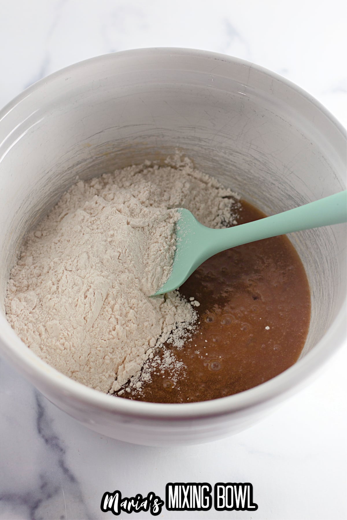 flour being added to wet batter in a mixing bowl.
