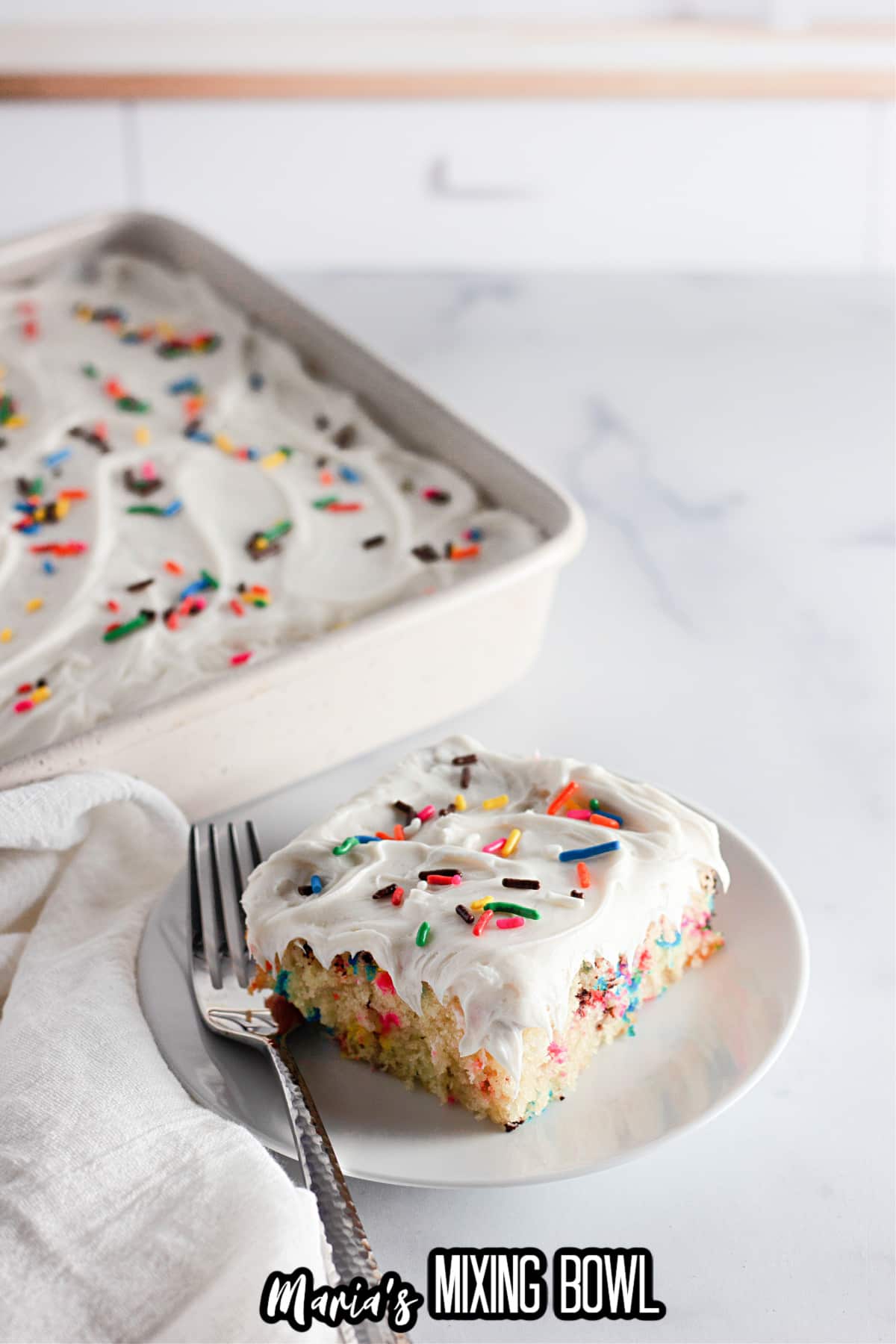 slice of funfetti cake on a white plate with a fork.