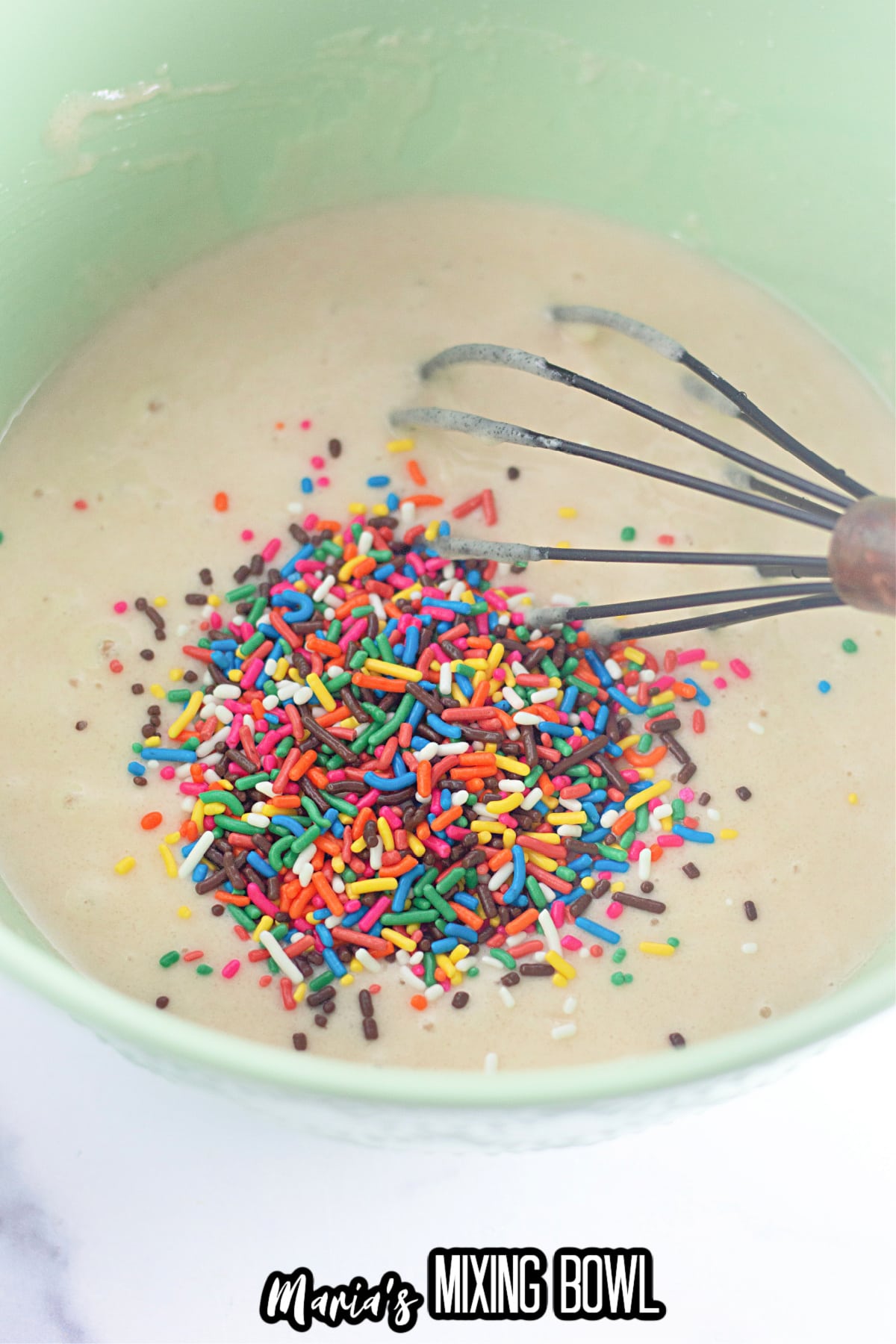 sprinkles being added to cake batter in a mixing bowl.