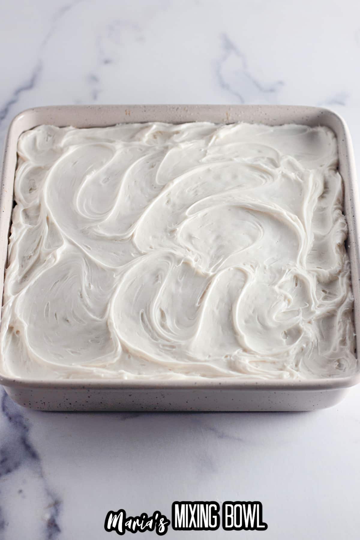 funfetti cake being frosted in a square baking dish.