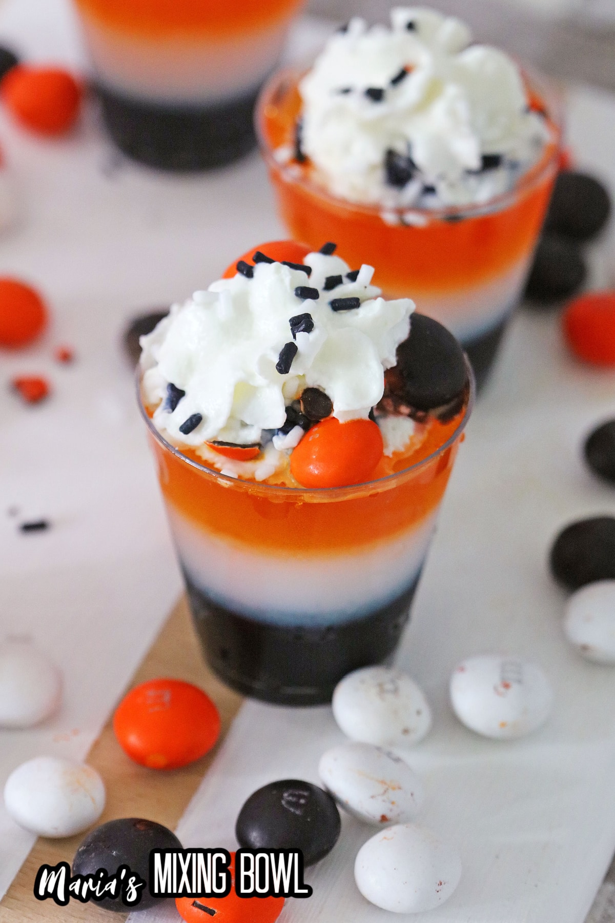layered halloween shots on a wooden cutting board surrounded by M&M's.
