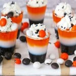 layered halloween shots on a wooden cutting board surrounded by M&M's.