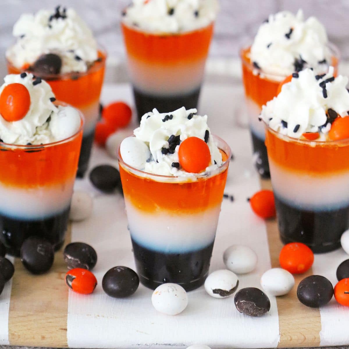 layered halloween shots on a wooden cutting board surrounded by M&M's.